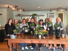 Group posing behind a wooden table with potted plants in a bright greenhouse or garden room
