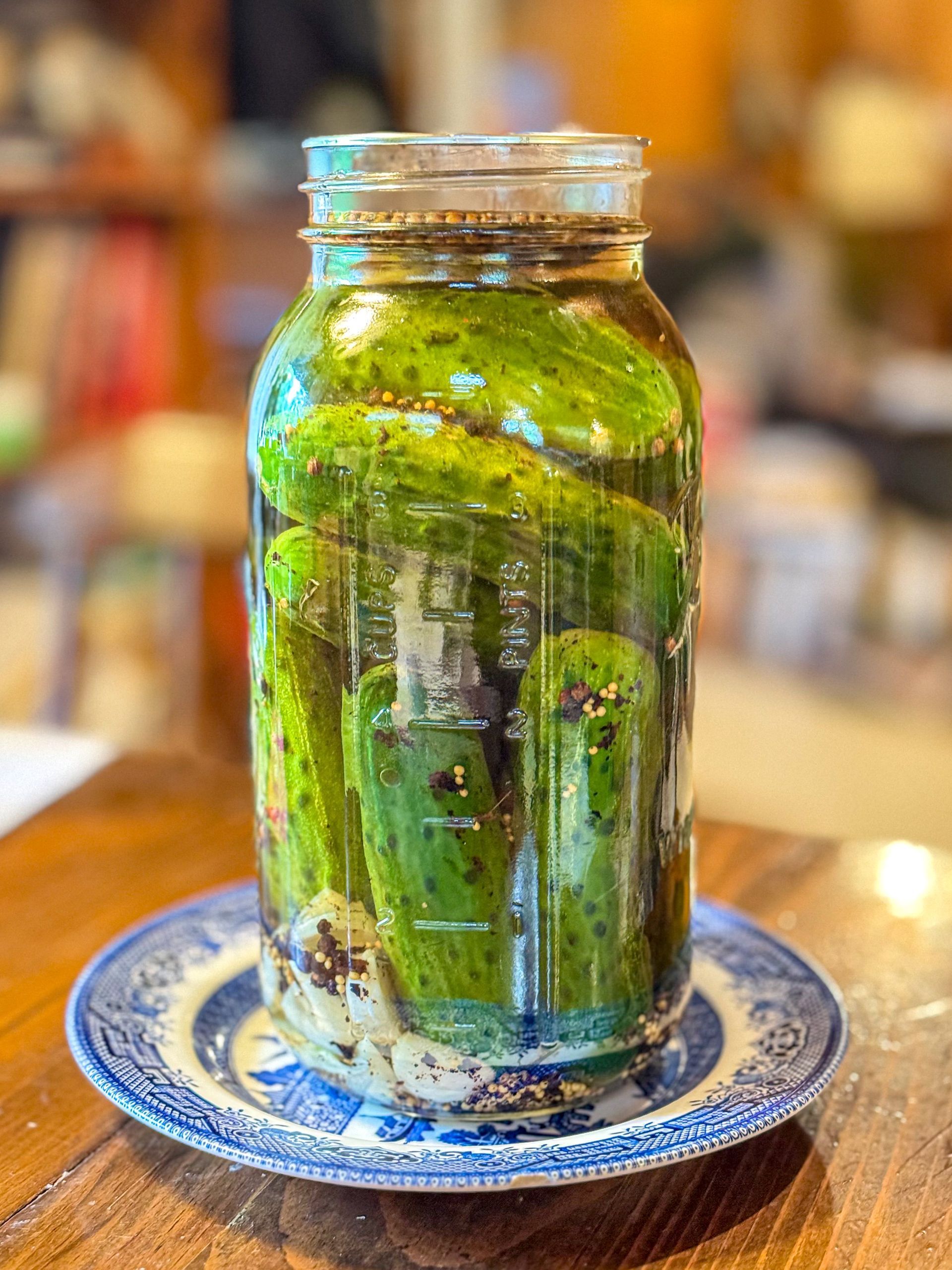 A green glass jar candle on a blue patterned saucer, with wax drips and a warm blurred background