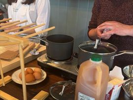 Hands cooking at a stovetop with a pot, eggs, and a jug of milk on the counter.