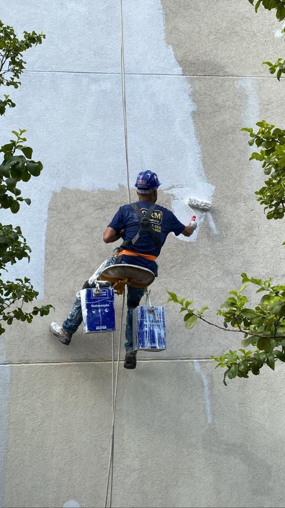 Um homem está pendurado em uma corda enquanto pinta uma parede