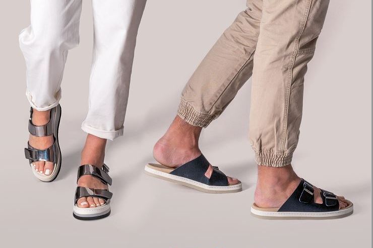 שני אנשים נועלים סנדלים, אחד כסוף, אחד כחול נייבי, עם מכנסיים לבנים וחומים, בתוך הבית.