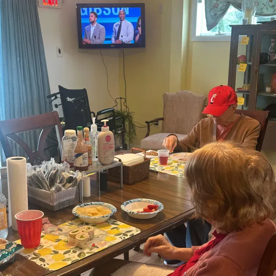 People seated around a dining table with snacks in a cozy living room, watching TV and eating.