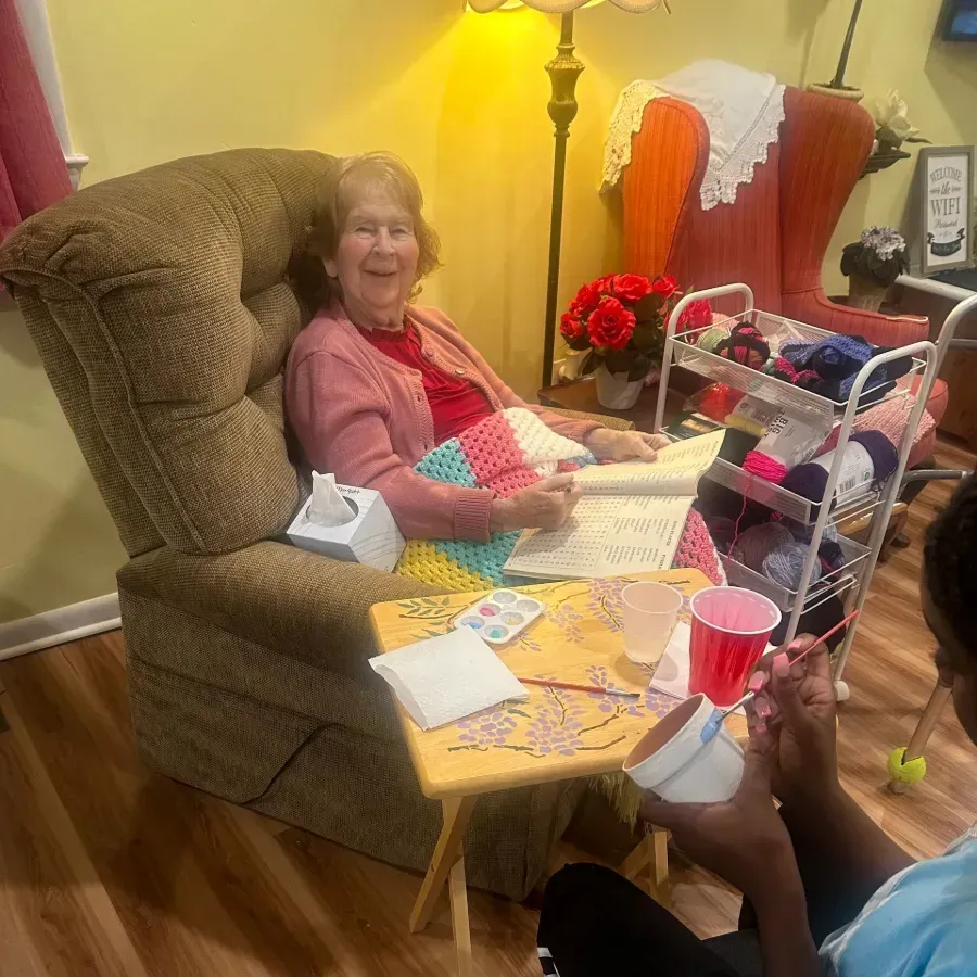 Smiling woman in a recliner with a craft table, yarn, and supplies in a cozy living room