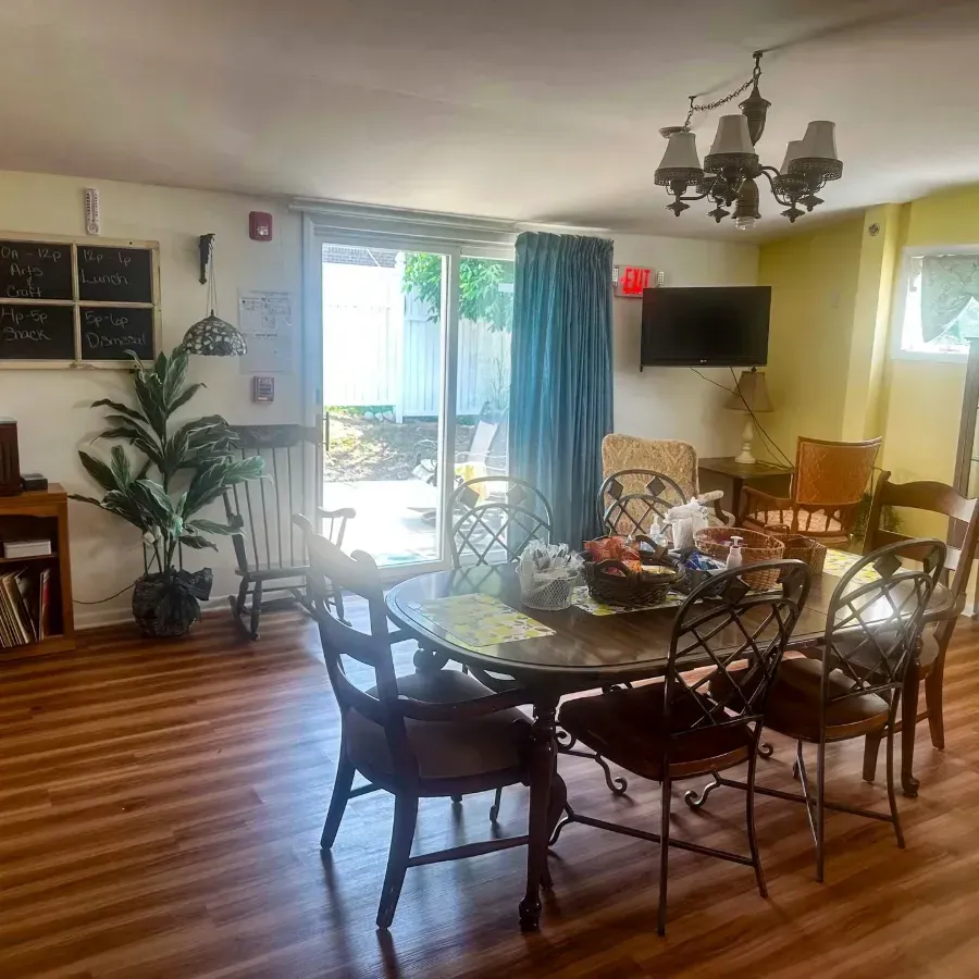Bright dining room with glass table, chairs, chandelier, plants, TV, and sliding doors to a patio
