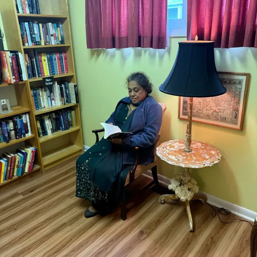 Person reading in a cozy library nook beside a lamp and bookshelf.