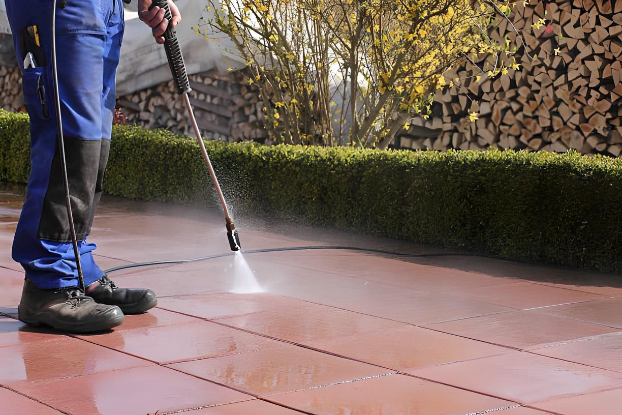 A man is using a high pressure washer to clean a brown patio