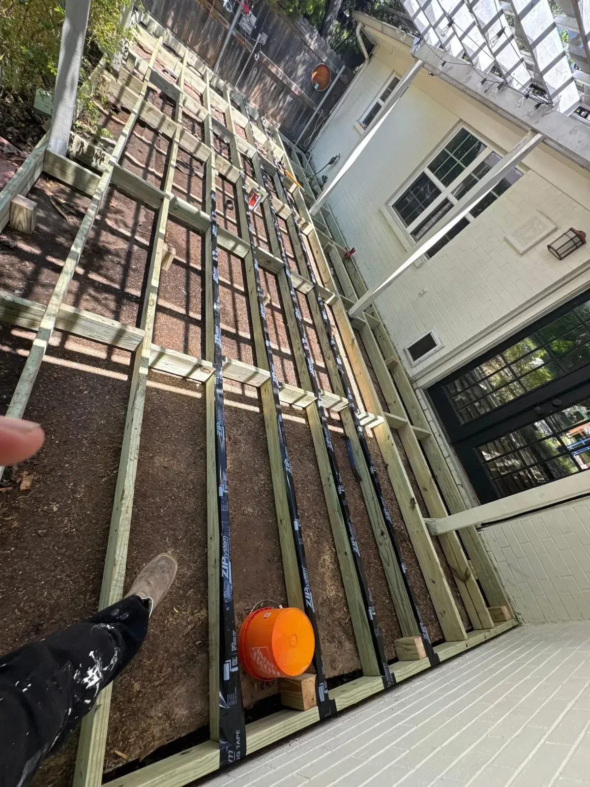A person is standing on a wooden deck under construction.