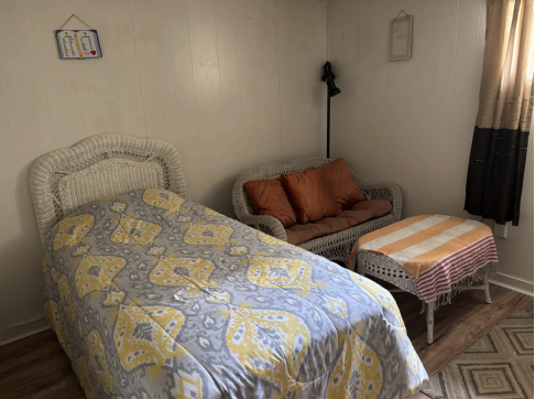 Small bedroom with a bed, loveseat, and plaid-covered table beside a curtained window.