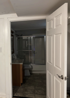Open white door leading to a bathroom with a glass shower and tiled floor.