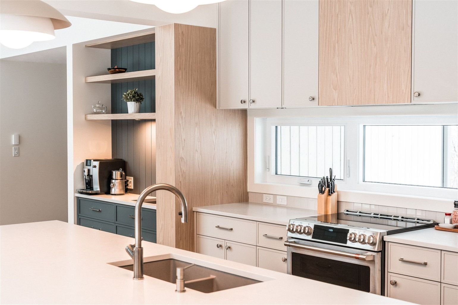 Une cuisine moderne avec des armoires de couleur claire, des touches de bois, un îlot central avec évier et une cuisinière en acier inoxydable.