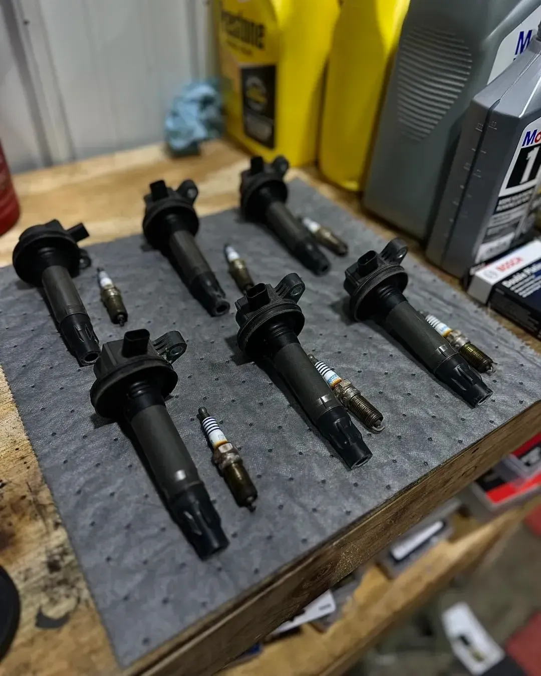 Six ignition coils and spark plugs arranged on a gray mat | Konstant Autowerks