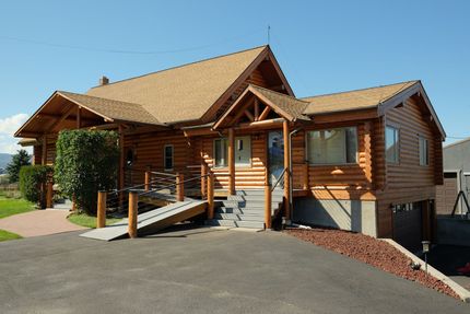 Wooden cabin-style house with porch, ramp, and stairs on a sunny day