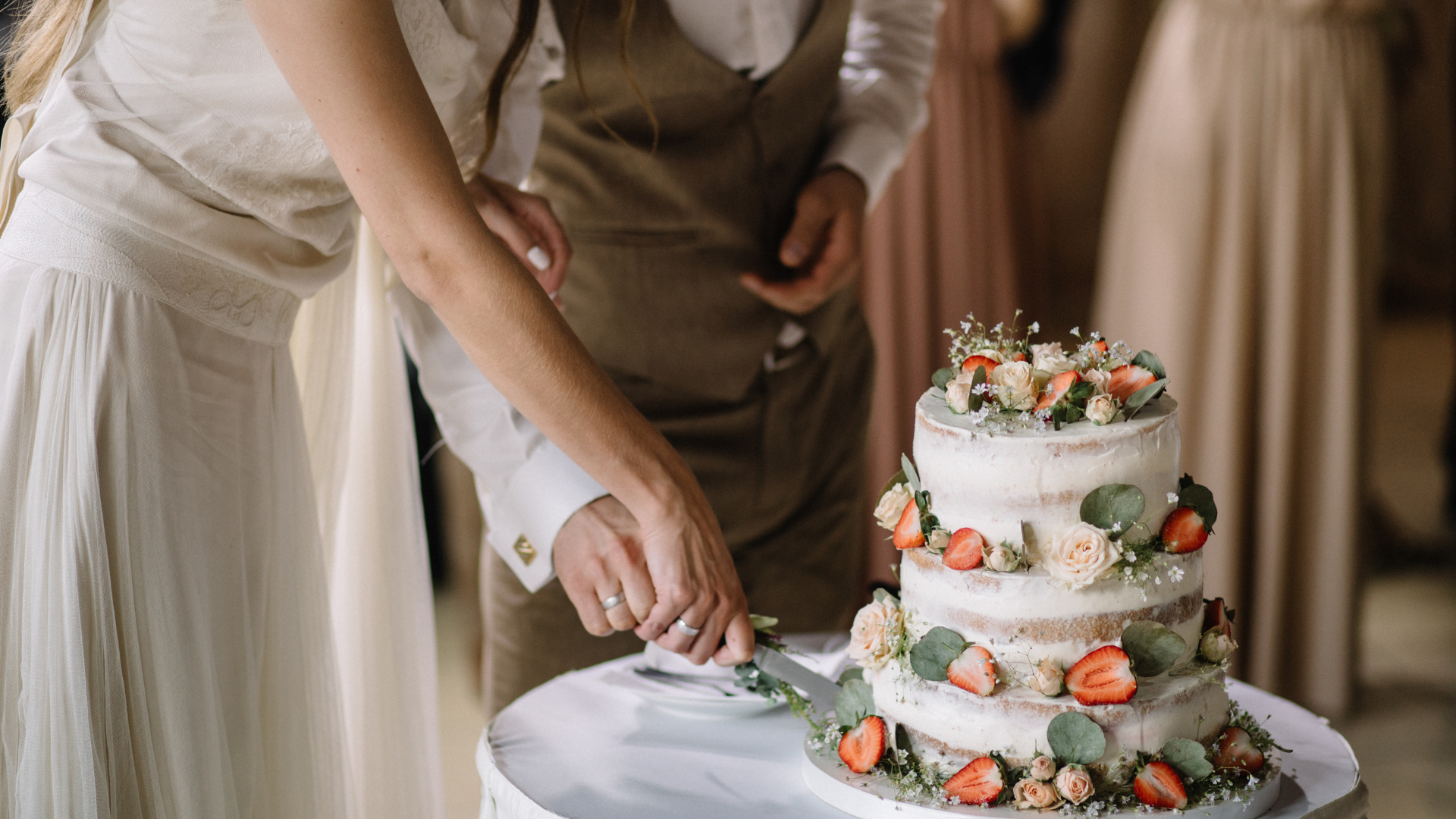 A bride and groom are cutting their wedding cake on a table.