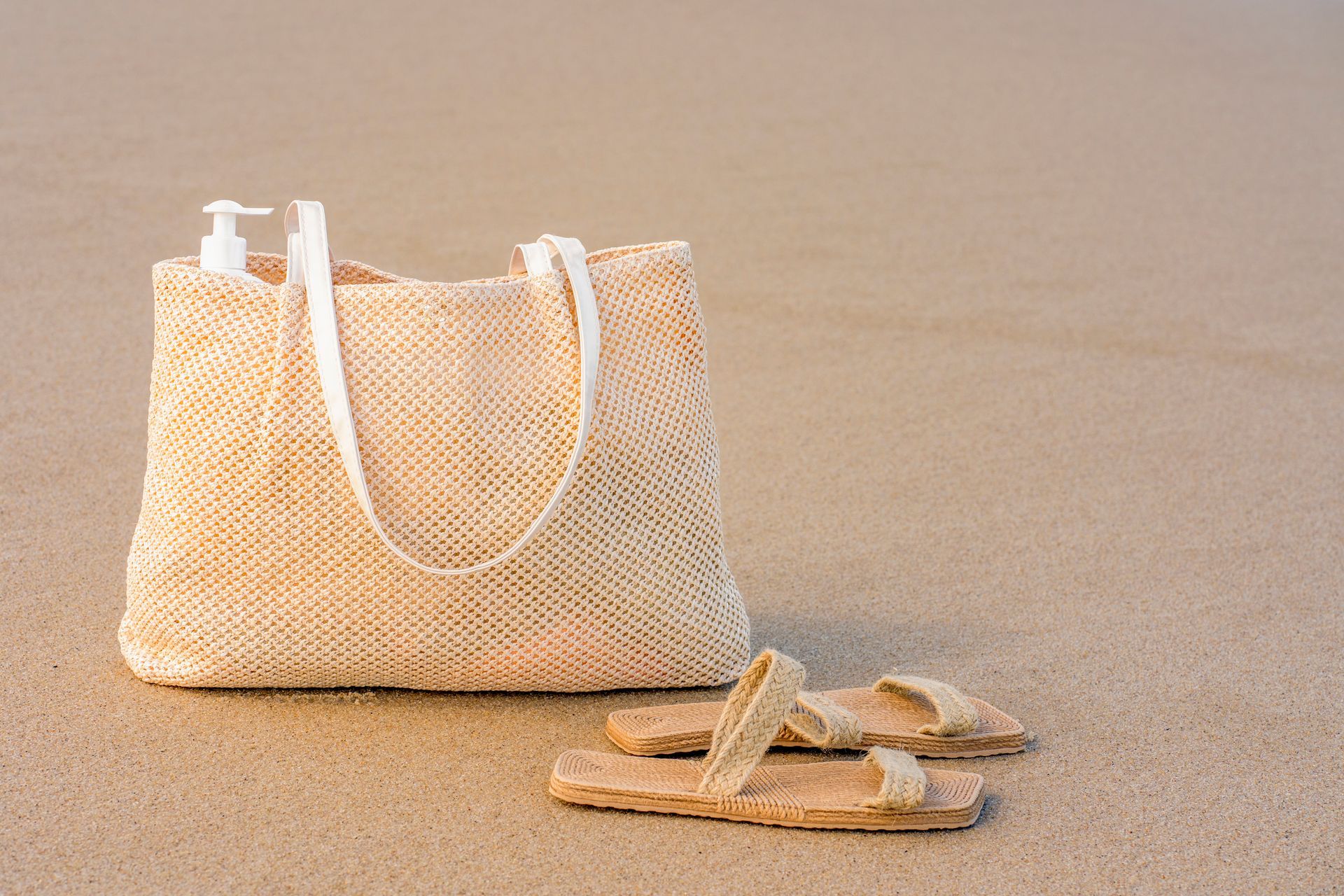 Una borsa di paglia e dei sandali sono sulla spiaggia.