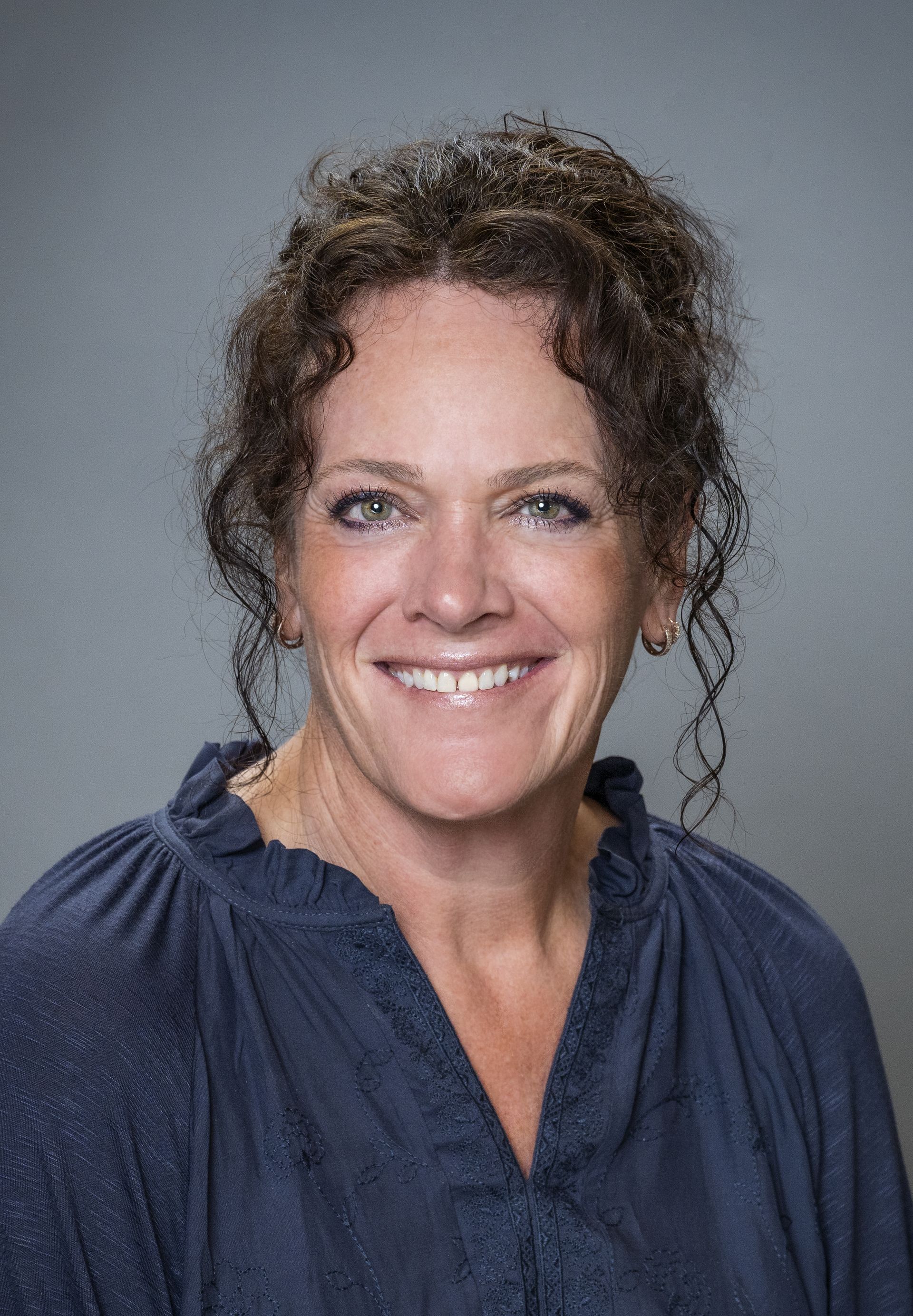 A woman in a black shirt is smiling in front of trees.