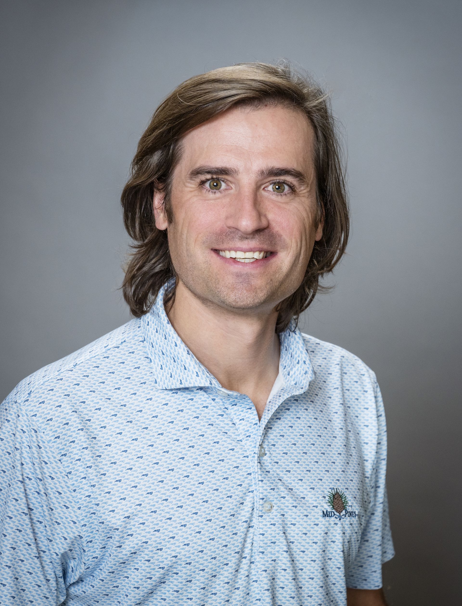 A man in a blue sweater is standing in front of trees.