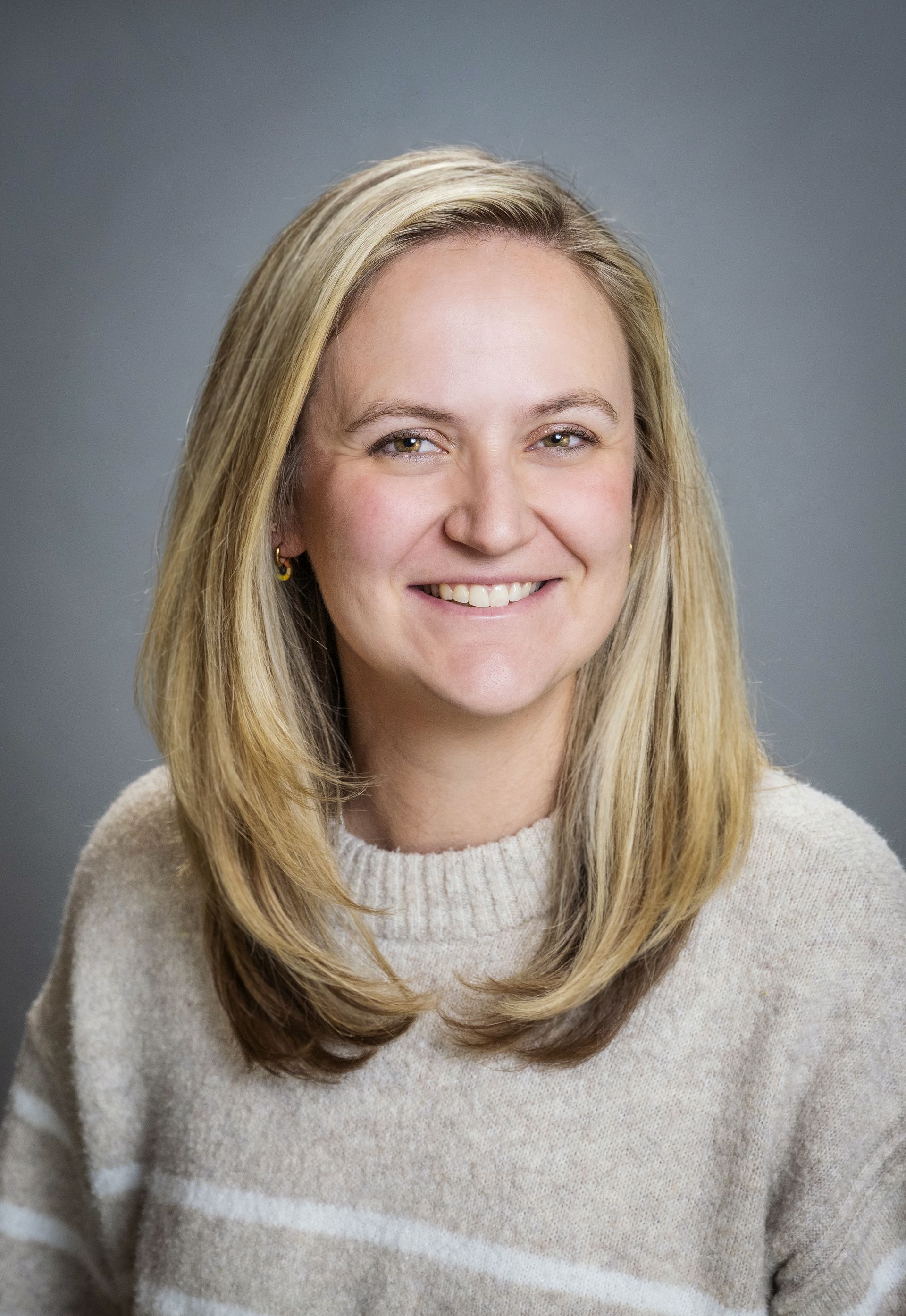 A woman in a blue shirt and necklace is smiling for the camera.