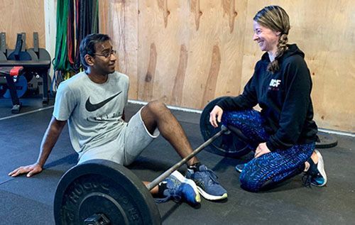 A man is sitting on the floor with a barbell and a woman is kneeling next to him.