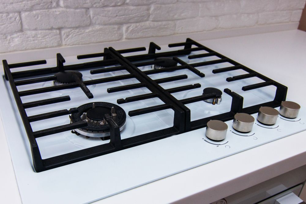 White and black gas cooktop with four burners and silver knobs, built-in on a white countertop.