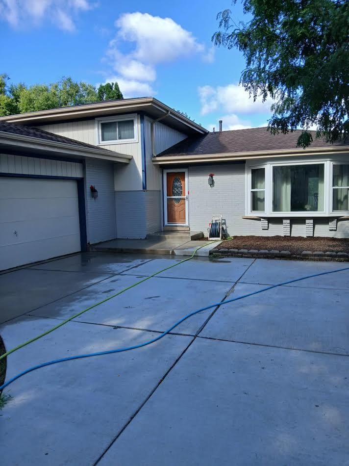 Gray house with a driveway. Blue sky, garage door, and brown front door.
