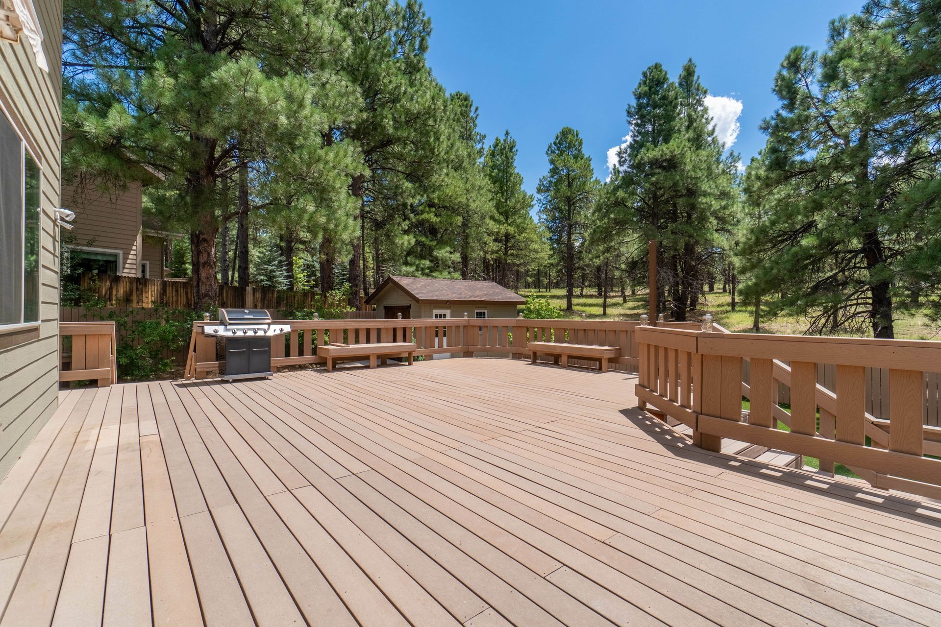 Wooden deck with a grill and benches, surrounded by trees.