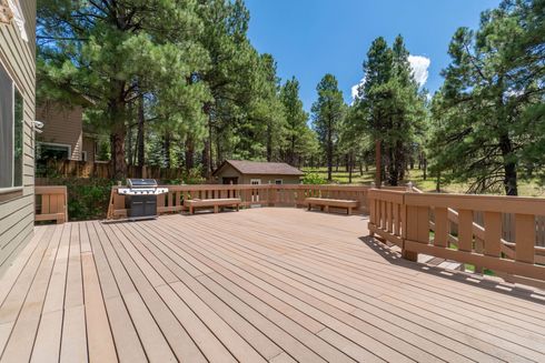 Wooden deck with a grill and benches, surrounded by trees.