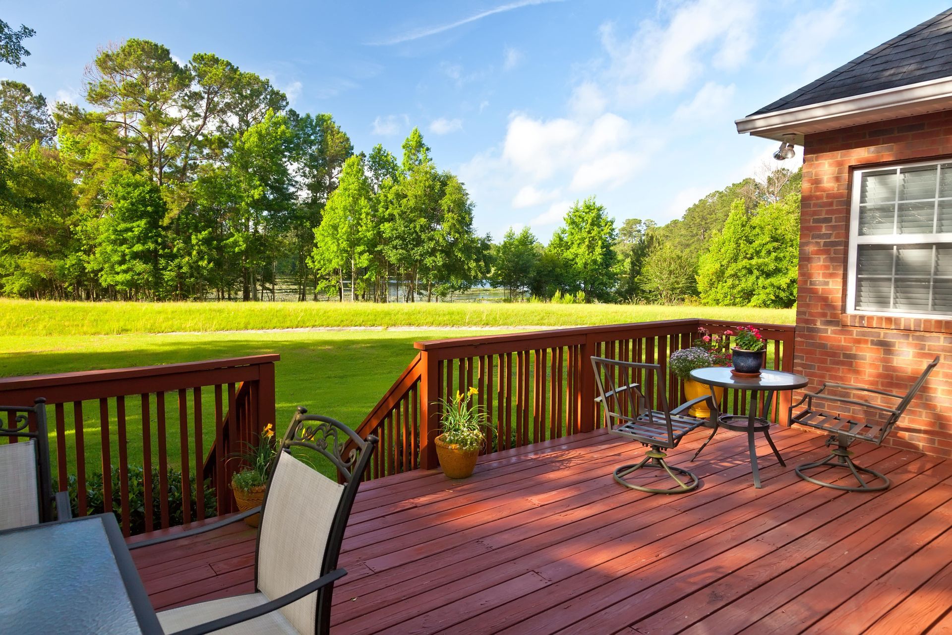 Wooden deck with patio furniture overlooking a grassy yard and trees under a blue sky.