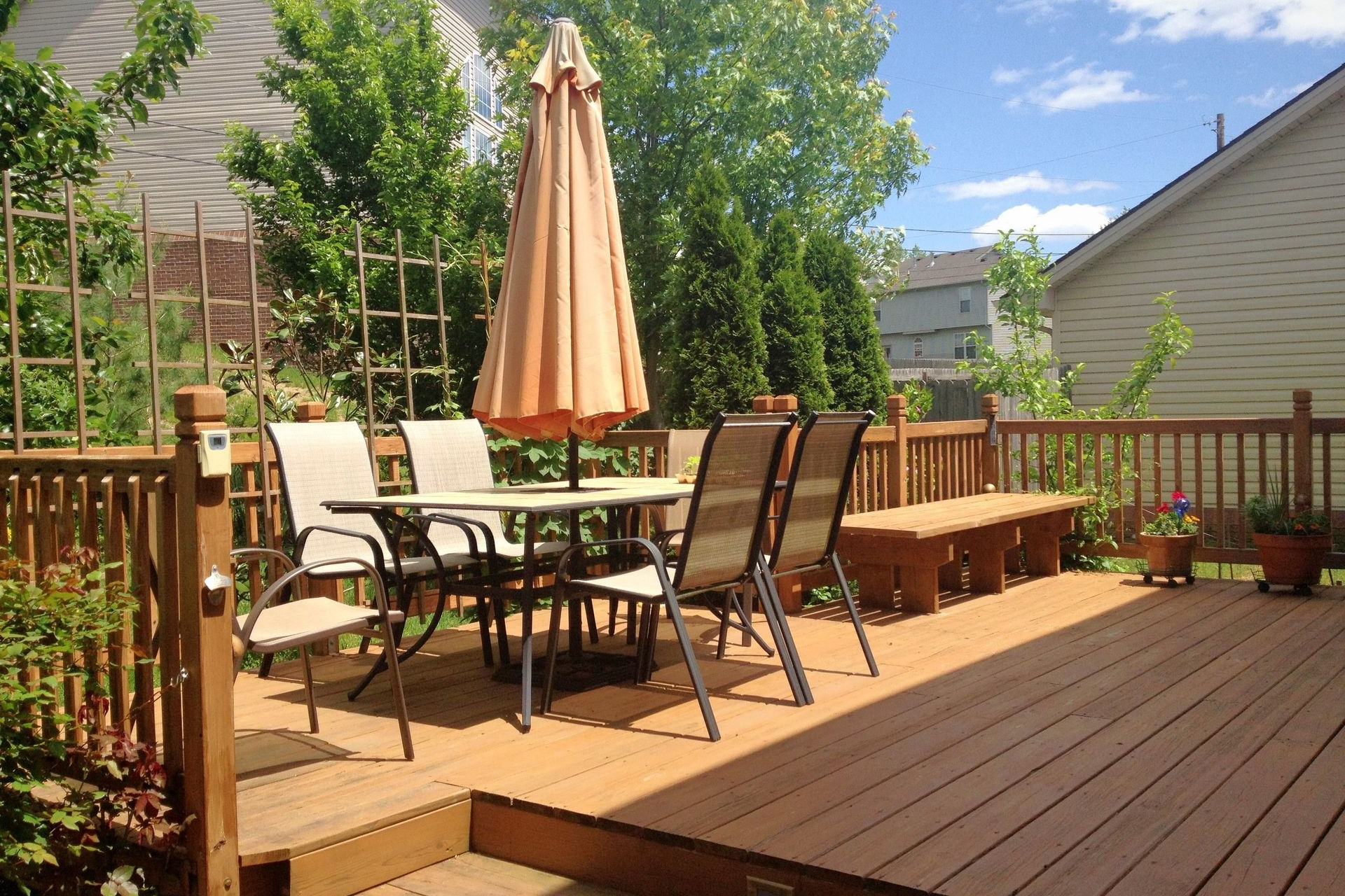 Wooden deck with patio table, chairs, and umbrella, sunny day.