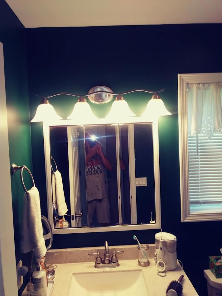 Bathroom with a dark green wall, mirror, vanity, and light fixture.