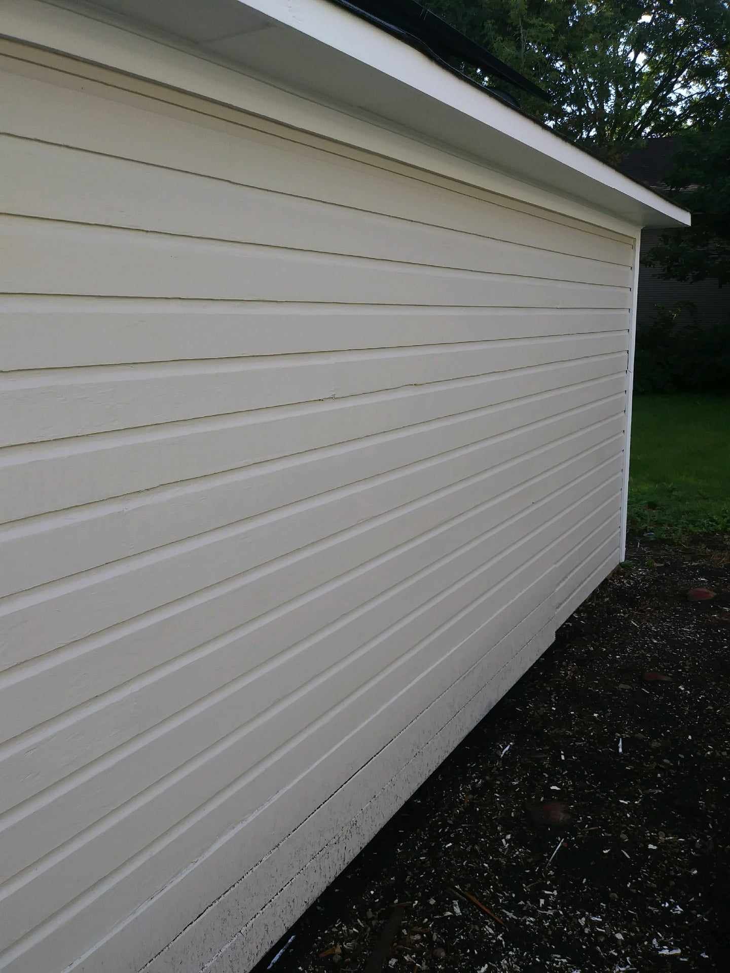 Off-white siding on a building with white trim. Dark ground and green grass in the background.
