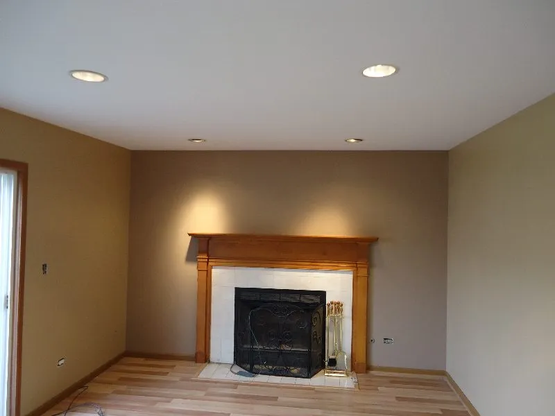 Fireplace in a room with tan walls, wood floor, recessed ceiling lights.