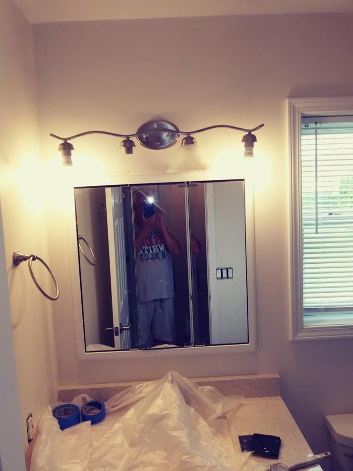 Bathroom with mirror, light fixture, and person reflected holding phone, near window and countertop.