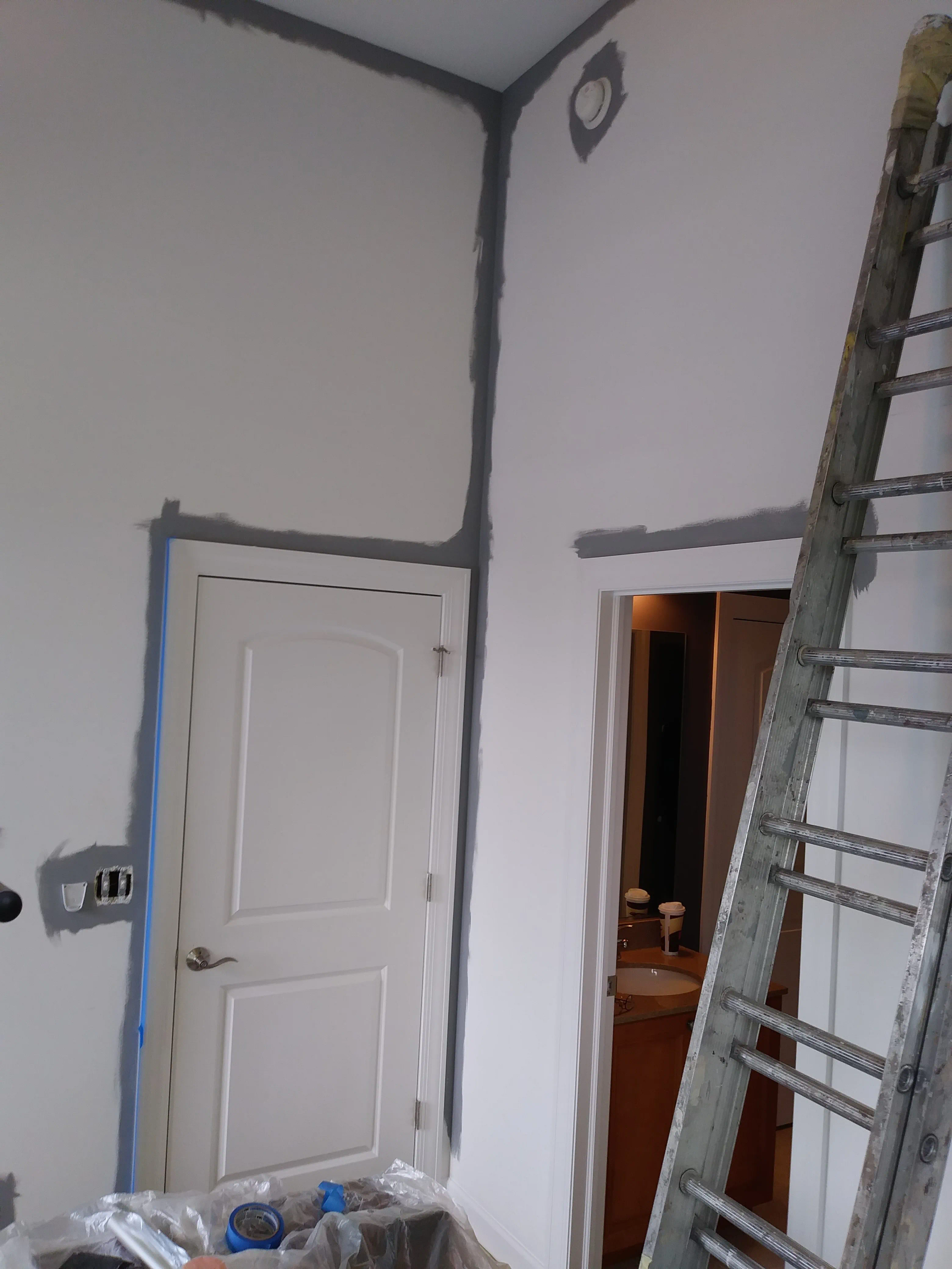 A room being painted, with a door and ladder. Grey tape around door and ceiling.