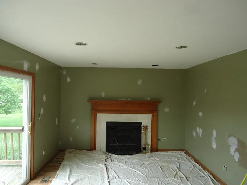 Interior room with olive green walls, fireplace, and patches of drywall. Ceiling has recessed lights.
