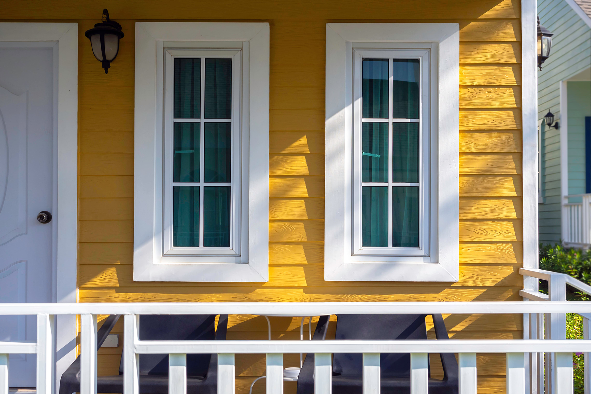 Yellow house exterior with white-framed windows, white railing, and door.