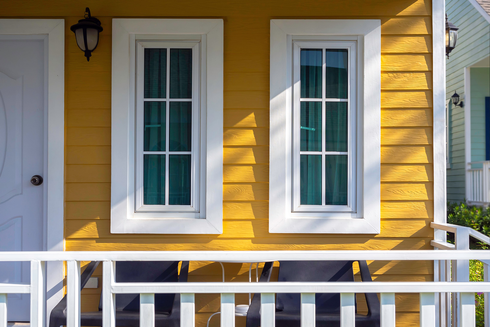 Yellow house exterior with white-framed windows, white railing, and door.
