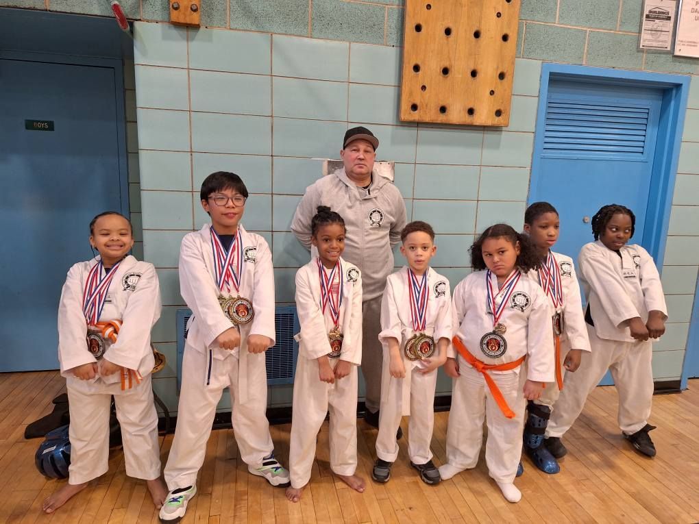 Group of young martial artists and instructor pose in a gym, all wearing medals and white uniforms.