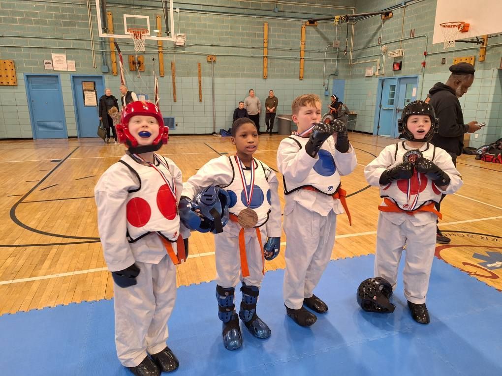 Young martial artists in safety gear stand in a gym, celebrating.