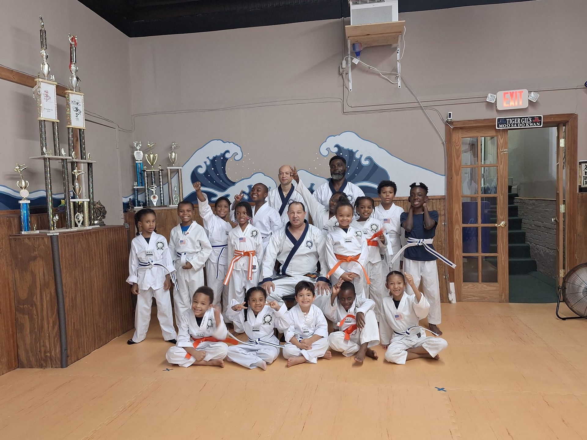 Group of kids in martial arts uniforms pose with instructor in dojo.