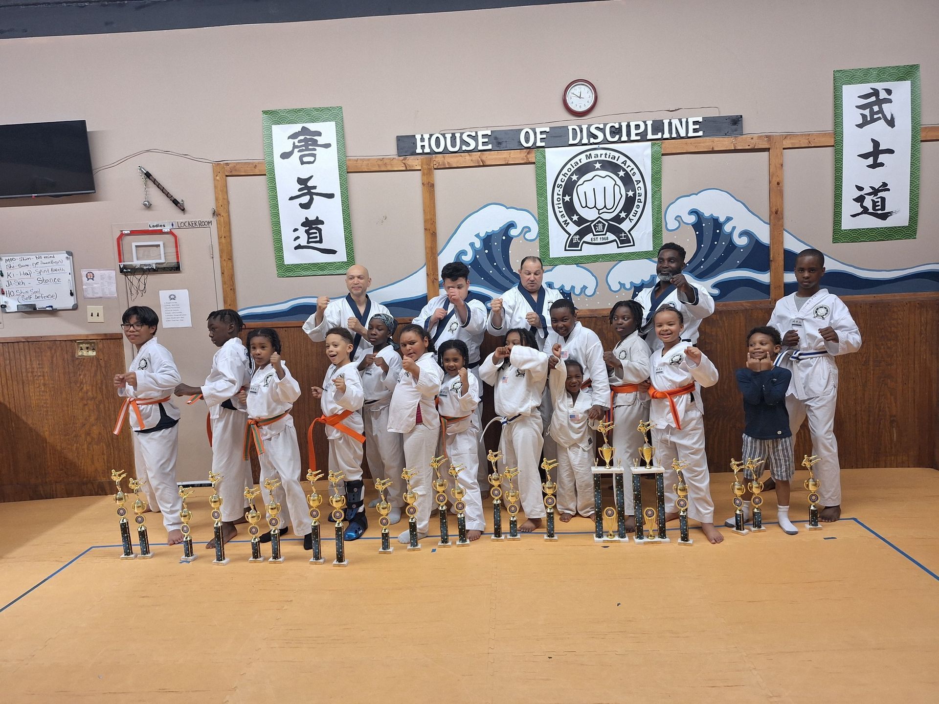 Martial arts students with trophies posing in a dojo, various ages and skin tones.