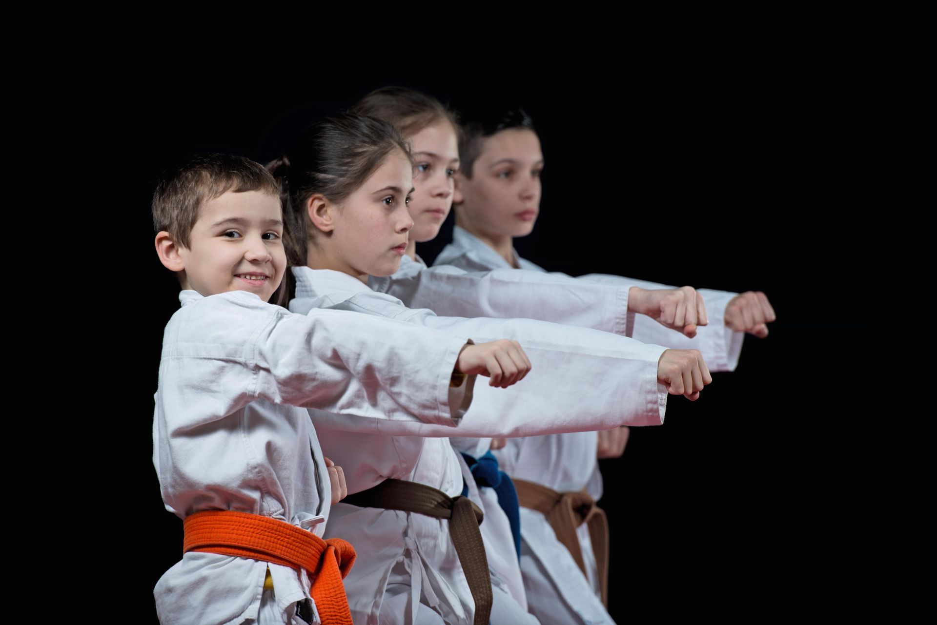 Children in karate uniforms practice punches, black background.