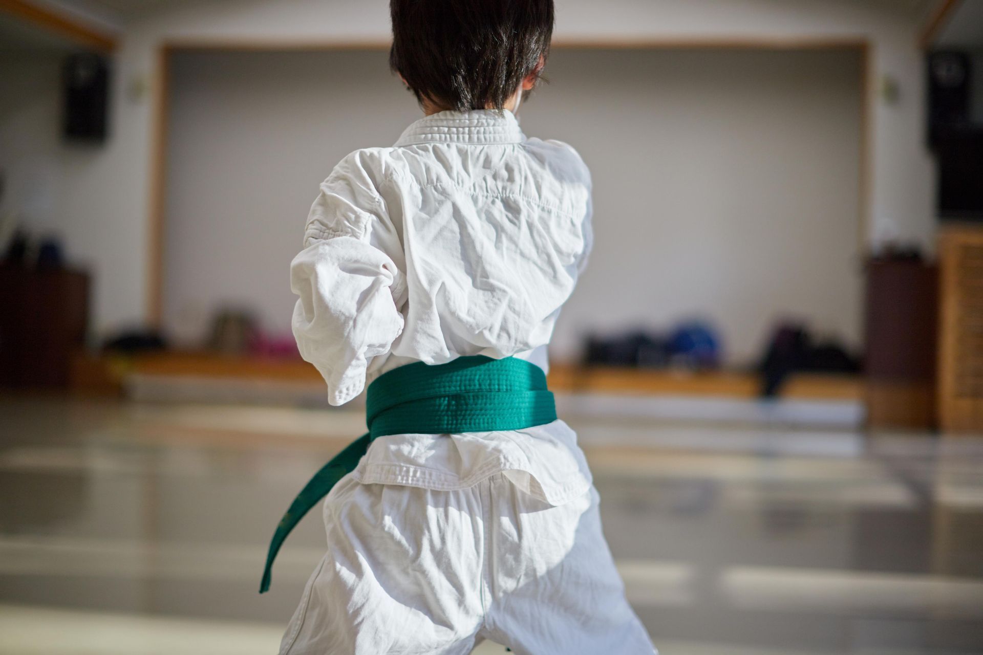 Child in karate uniform with green belt, in a dojo, practicing a karate stance.