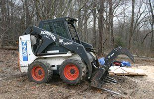 A bobcat skid steer with a grapple attached to it is parked in the dirt.