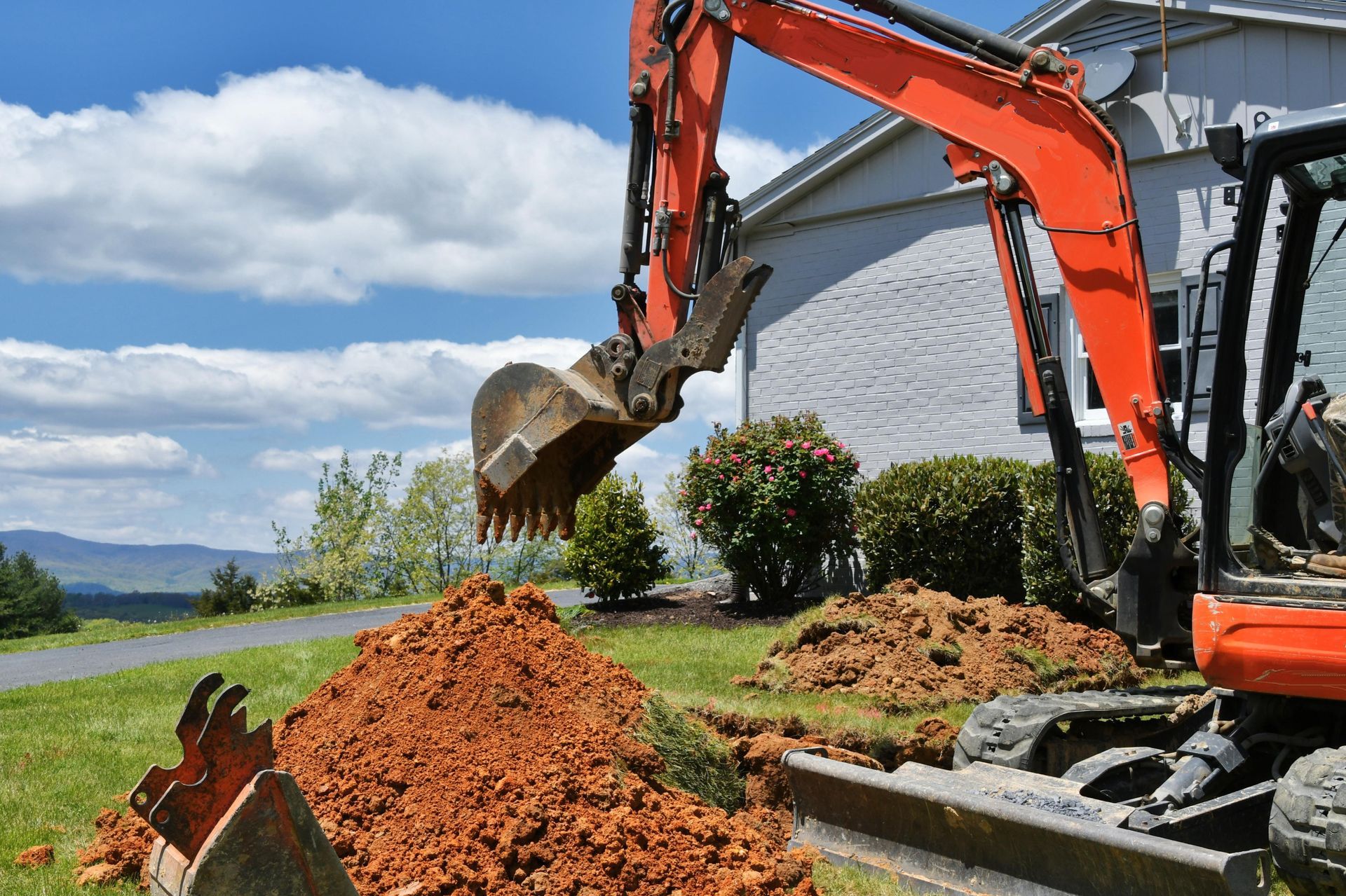 An excavator is digging a hole in the ground in front of a house.