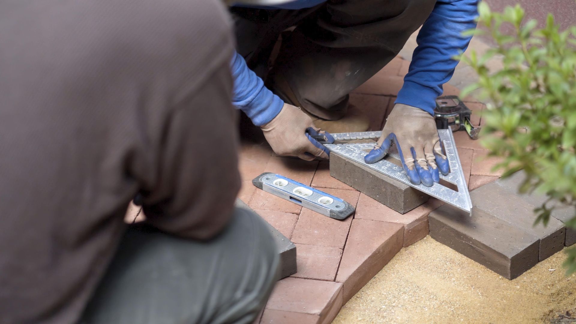 Two men are working on a brick walkway.