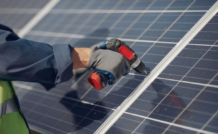 Un hombre está trabajando en un panel solar con un taladro.