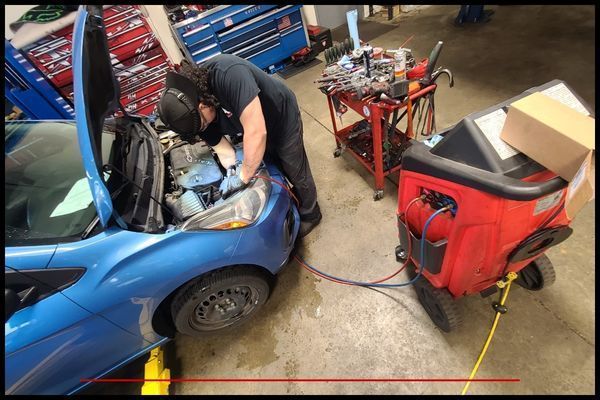 Mechanic working on a blue car engine with equipment in a garage. | Integrated Automotive