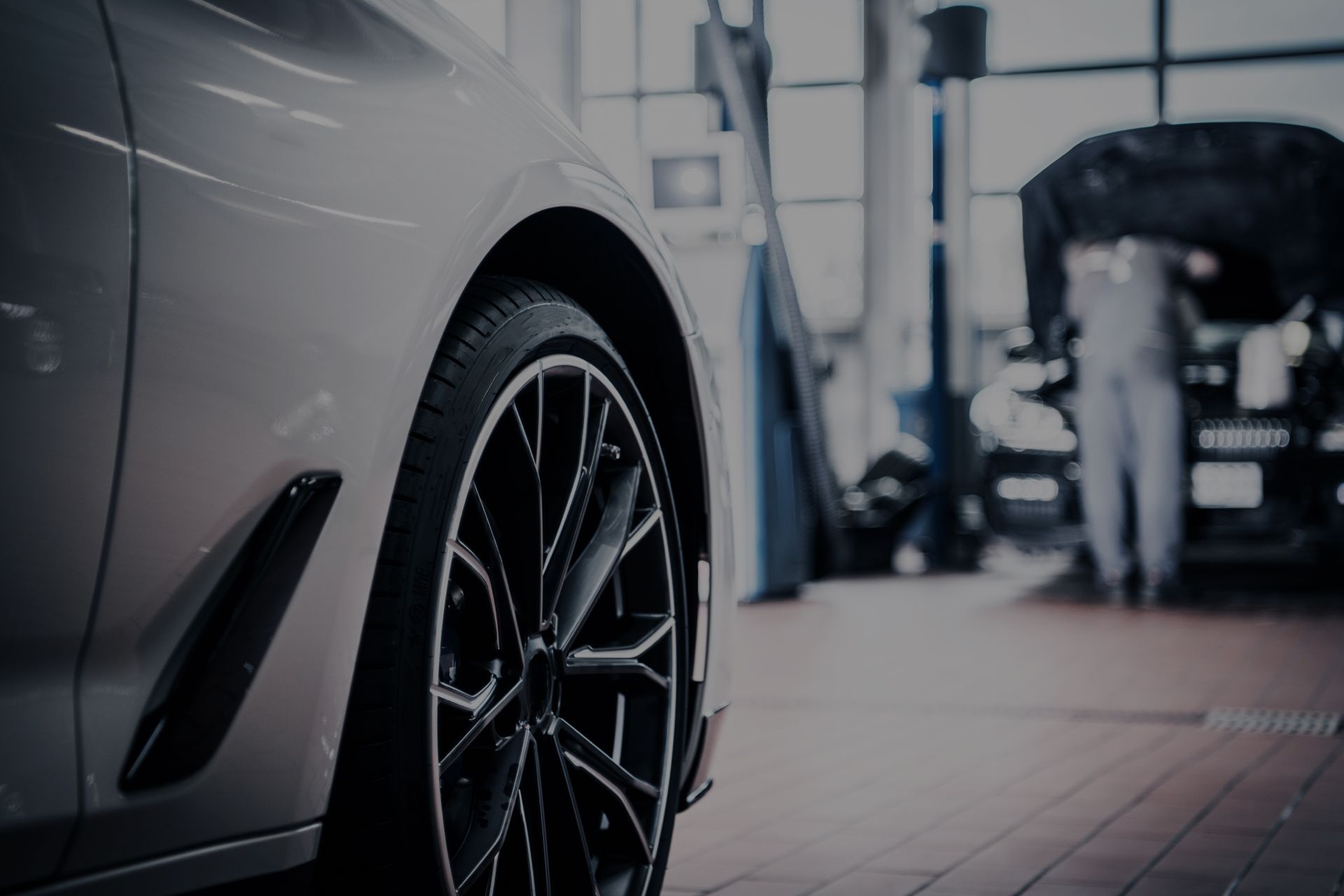 Close-up of a silver car wheel in an auto repair shop with a mechanic working on another car in the background | Integrated Automotive
