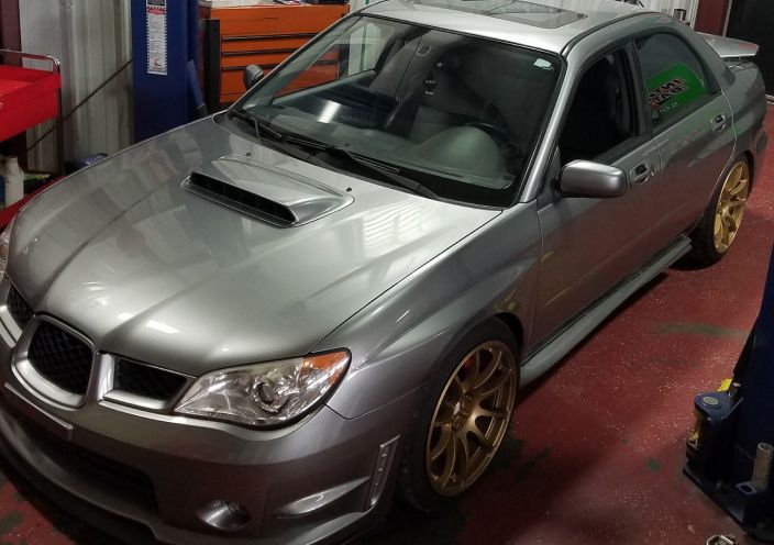 A silver Subaru WRX sedan with gold wheels parked inside an auto shop. | Integrated Automotive