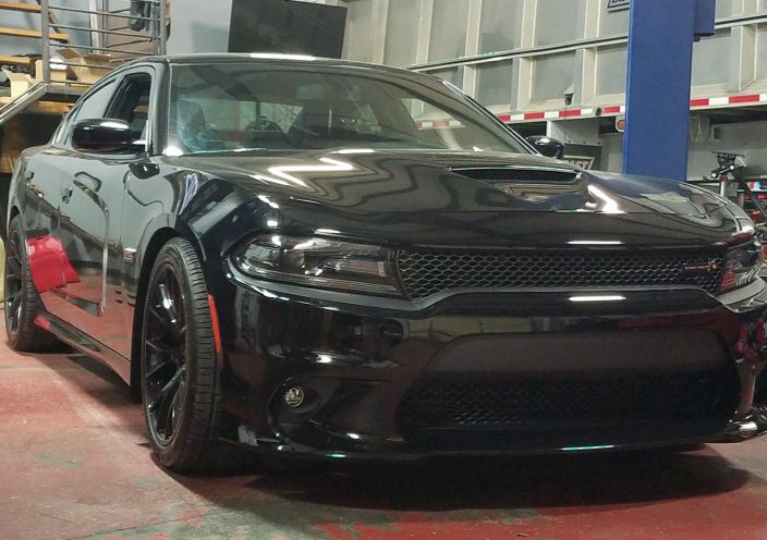 A black Dodge Charger parked in a garage with a front-facing view of its hood scoop and honeycomb grille. | Integrated Automotive
